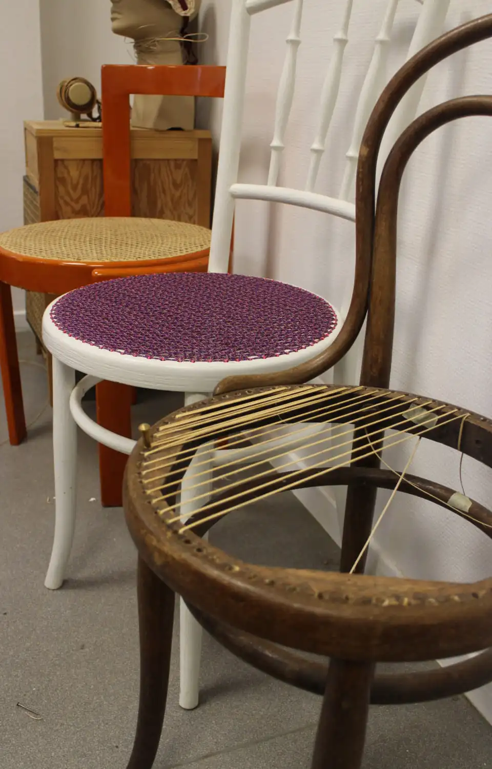 Photos de chaises dans l'atelier. Une chaise est restaurée en canage, une est modernisée en cordelette de couleur violette. La chaise au premier plan est une chaise de bistro Thonet en cours de restauration.