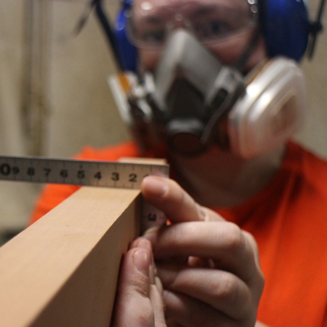 Photo dans l'atelier d'ébénisterie de la CoFabrik. Inès avec les EPI en train de vérifier l'équerrage d'une traverse.