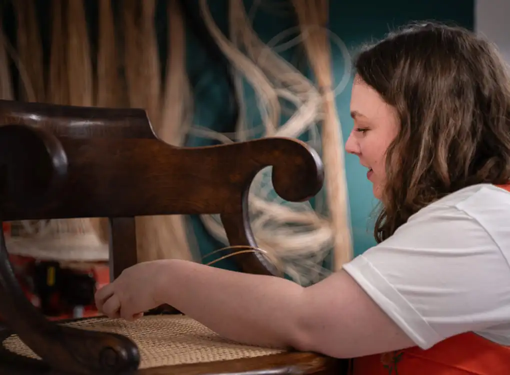 Inès Hayaud en train de restaurer une fauteuil de Maire en cannage de manière traditionnel. Photo prise dans son atelier par Nathalie Rodriguez