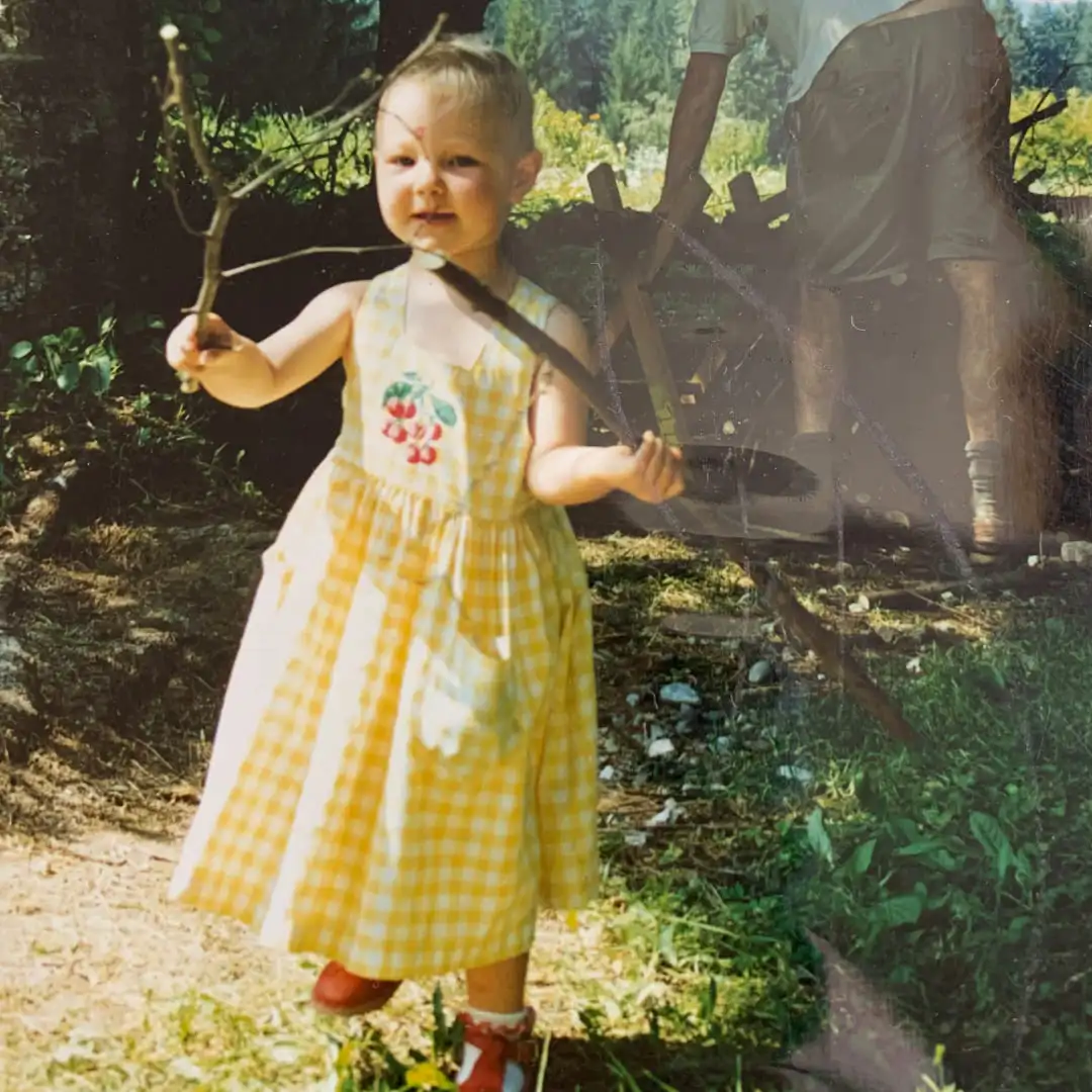 Photo d'un souvenir d'enfance. Inès en robe avec des branche de bois dans les mains. Les souvenirs sont ses sources d'inspiration dans la création. 