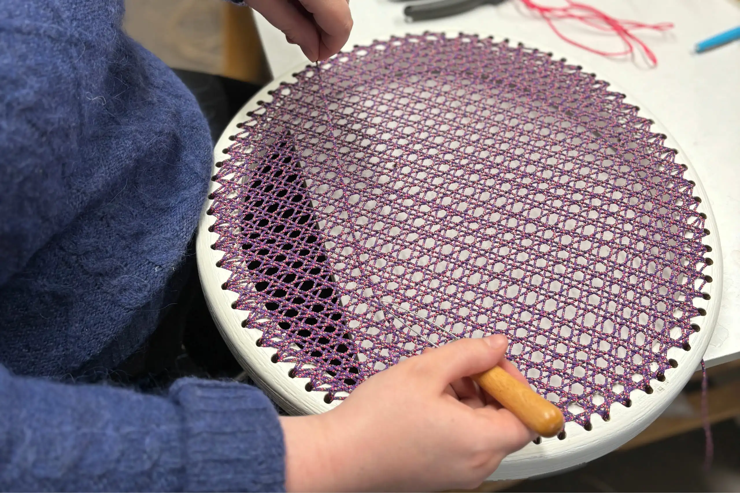 Photo d'Inès Hayaud en train de tisser dans son atelier lillois une assise canné en cordelette de couleur violette.
