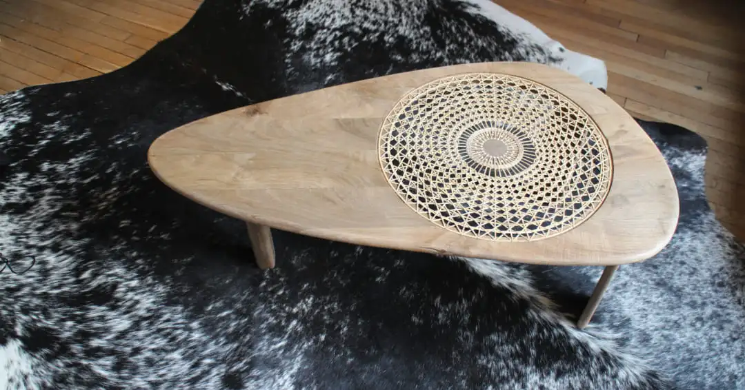 Table basse en cannage soleil et noyer européen. Table de forme triangulaire avec chant arrondi et 3 pieds.